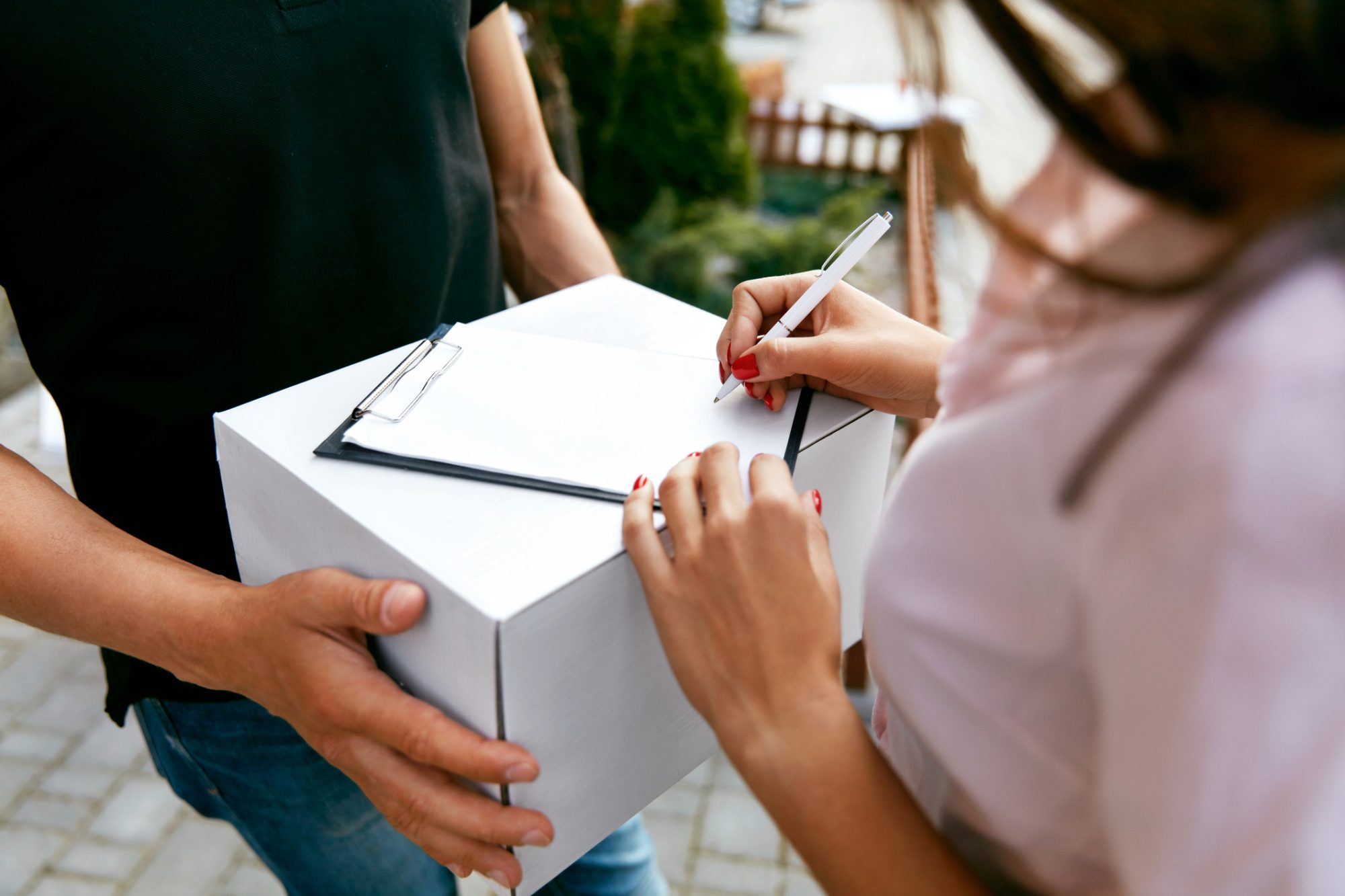 Express Delivery. Courier Delivering Package To Woman. Closeup Female Hands Signing Delivery Document On Box. High Resolution