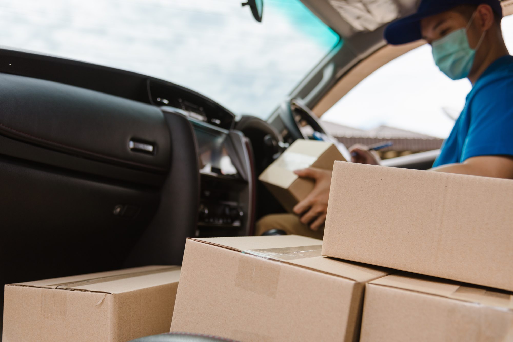 Asian delivery courier young man driver inside the van car with parcel post boxes checking amount he protective face mask, under curfew quarantine pandemic coronavirus COVID-19